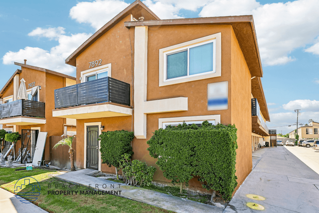 A two-story house with a balcony and a front yard with a hedge.